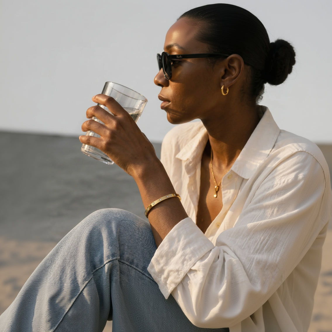 Mein Shop gold bangle bracelet with clear stones, worn by a woman in a white shirt and sunglasses.