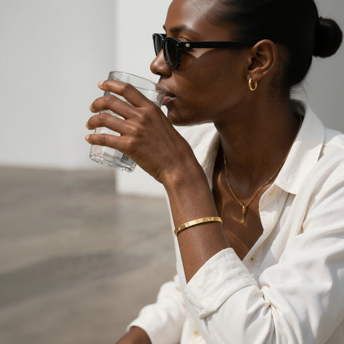 Mein Shop gold bangle bracelet with clear stones, worn by a woman drinking water.