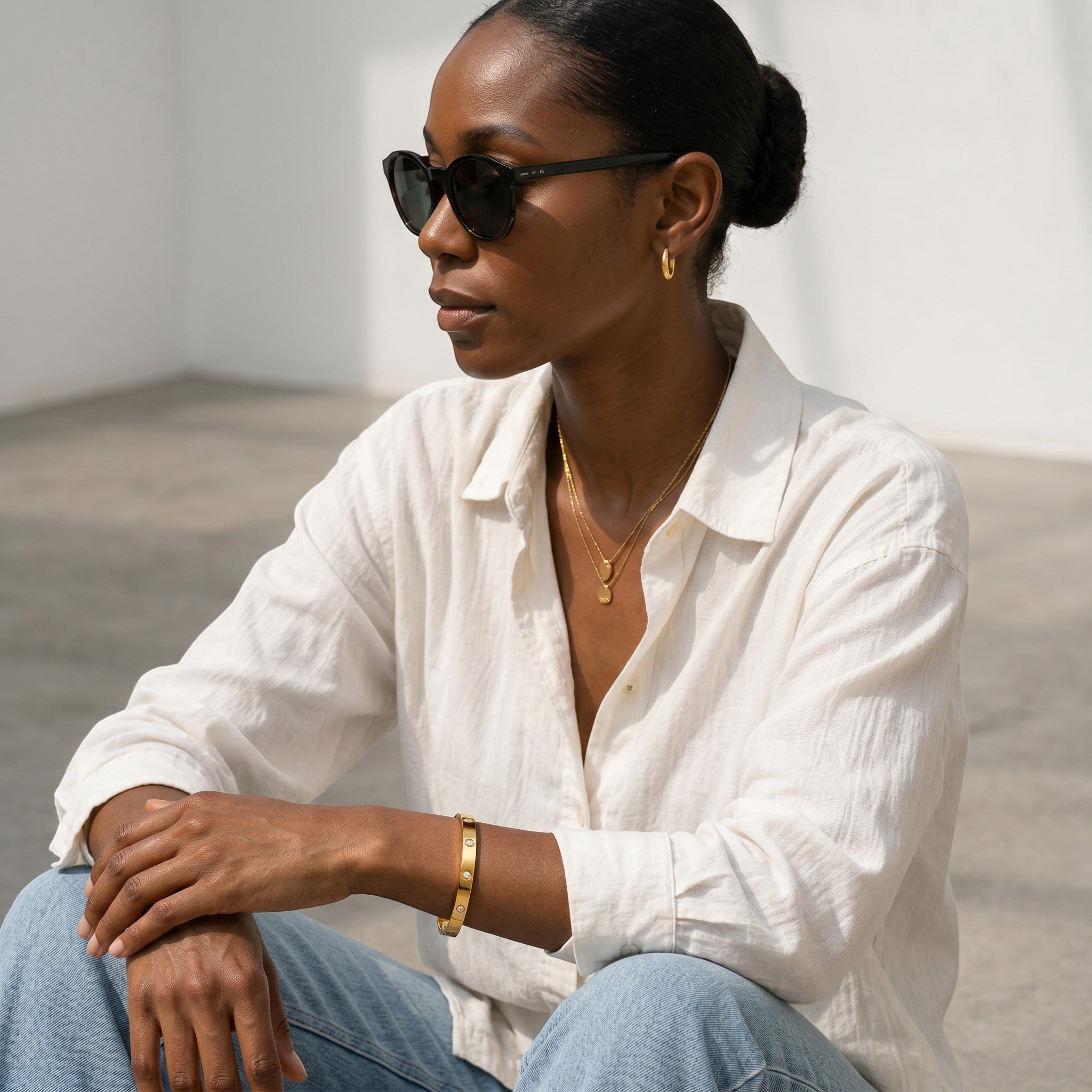 Mein Shop gold bangle with clear stones and gold chain necklace on a woman wearing sunglasses and a white shirt.