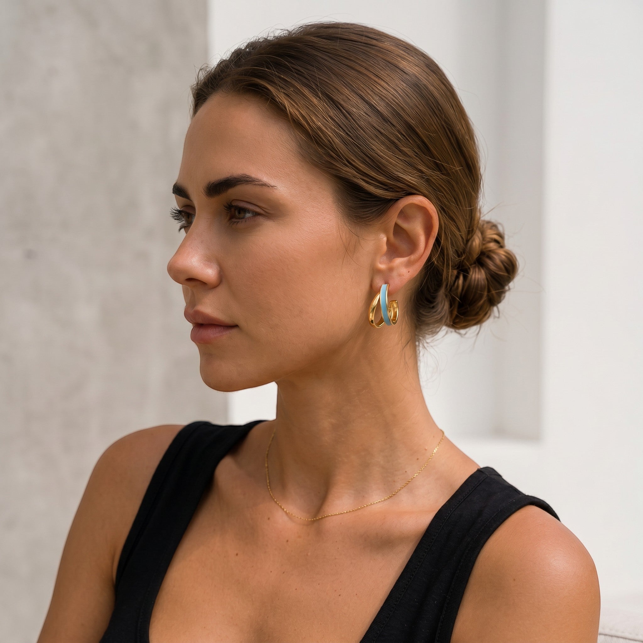 Mein Shop gold hoop earrings with light blue enamel detail, worn by a woman with her hair in a bun.